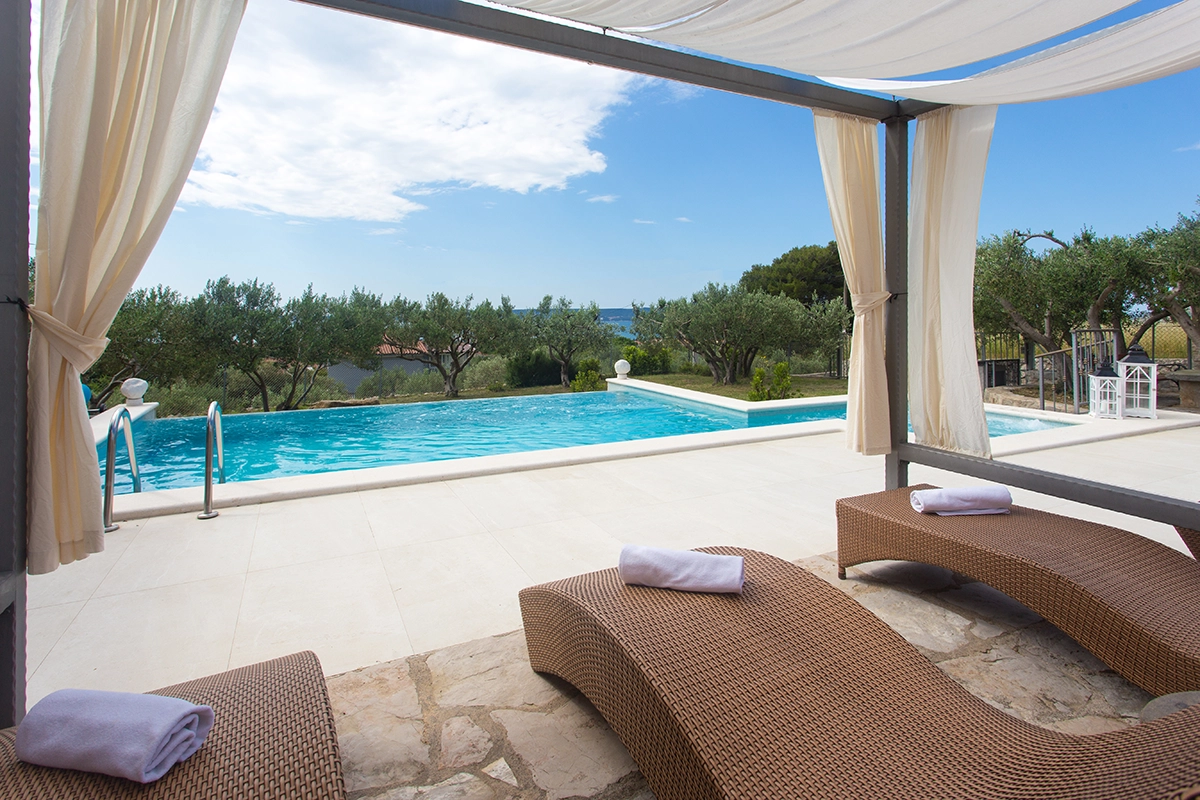 Bird's-eye view of the villa, pool, sun loungers, entire paved yard, garden, and olive trees.